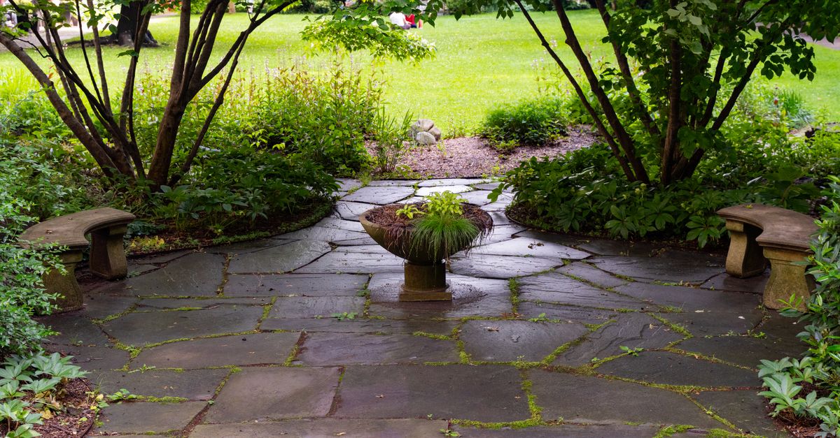 Peaceful stone patio surrounded by greenery and a central plant centerpiece in a New York garden.